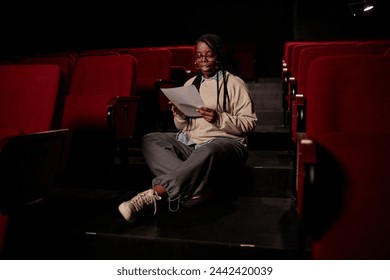 Full length portrait of Black female artist reading lines sitting on floor in theater copy space - Powered by Shutterstock