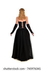 full length portrait of a blonde girl wearing black gothic gown, standing pose isolated on white background.