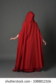 full length portrait of brunette girl wearing red fantasy costume with cloak, standing pose on a guy studio background.