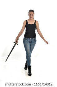 
full length portrait of brunette girl wearing black single and jeans. standing pose, holding a sword. isolated on white studio background.
