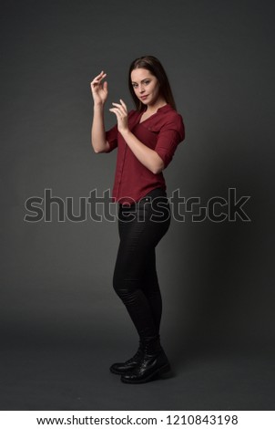  full length portrait of brunette girl wearing  red shirt and leather pants. standing pose , on grey studio background.