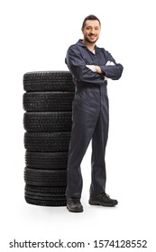 Full Length Portrait Of A Car Mechanic Posing With A Pile Of Tires Isolated On White Background