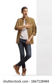 Full length portrait of a casual man in checkered shirt and jeans leaning on a wall and pointing to the side isolated on white background - Shutterstock ID 1867128484
