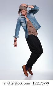full length portrait of a casual young man balancing on his toes while looking down and holding his hand on his head. on gray studio background