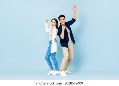 Full length portrait of cheerful Asian couple standing back to back smiling and clenching fists in light blue isolated studio background