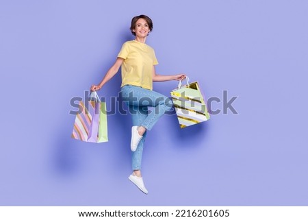 Full length portrait of cheerful energetic person jumping hands hold packages isolated on purple color background