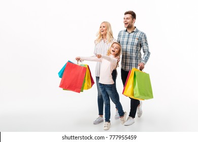 Full Length Portrait Of A Cheerful Family Holding Paper Shopping Bags While Walking Isolated Over White Background