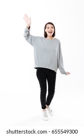 Full Length Portrait Of A Cheerful Girl Waving Hand To Camera Isolated Over White Background