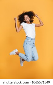 Full length portrait of a cheerful young african woman celebrating success while jumping isolated over yellow background