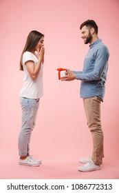 Full Length Portrait Of A Cheerful Young Man Giving His Girlfriend A Present Isolated Over Pink Background