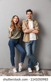 Full length portrait of a cheerful young couple standing together showing ok isolated over gray