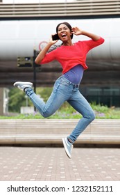 Full Length Portrait Of Cheerful Young Black Woman Jumping In The Air With Mobile Phone