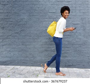 Full Length Portrait Of A Cheerful Young African Woman Walking On Street With A Mobile Phone