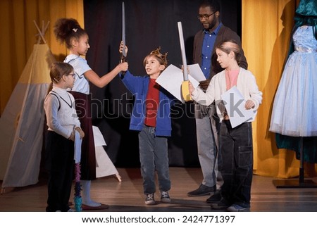 Full length portrait of children rehearsing school play on stage in theater with little boy prince reciting lines