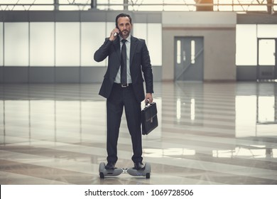 Full length portrait of concentrated bearded businessman talking by mobile while standing on giroscooter. Career and digital device concept - Shutterstock ID 1069728506