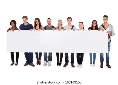 Full length portrait of confident multiethnic college students displaying blank billboard against white background - Powered by Shutterstock