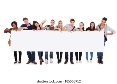 Full length portrait of confident multiethnic college students displaying blank billboard against white background - Powered by Shutterstock