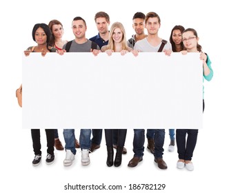 Full length portrait of confident multiethnic college students displaying blank billboard against white background - Powered by Shutterstock