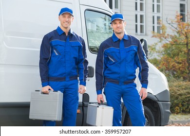 Full length portrait of confident technicians standing against truck on street