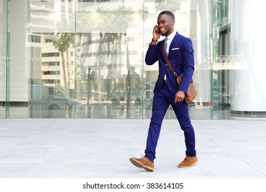 Full length portrait of a confident young businessman walking in the city talking on cell phone 