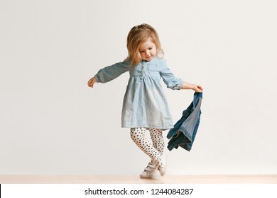 Full length portrait of cute little kid girl in stylish jeans clothes looking at camera and smiling, standing against white studio wall. Kids fashion concept - Shutterstock ID 1244084287