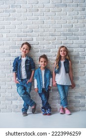 Full length portrait of cute little kids in stylish jeans clothes looking at camera and smiling, standing against white brick wall - Shutterstock ID 2223996259
