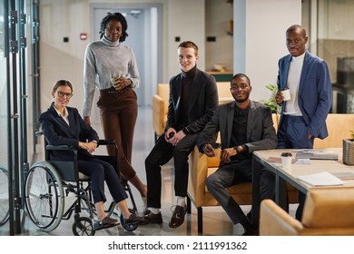 Full length portrait of diverse business team with young woman in wheelchair all smiling at camera in office