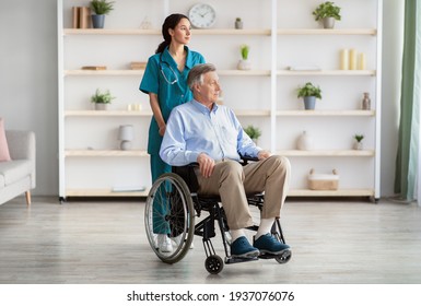 Full Length Portrait Of Elderly Male Patient In Wheelchair And His Young Caregiver At Retirement Home