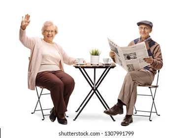 Full length portrait of an elderly woman sitting at a table with a cup of coffee and waving and an elderly man reading a newspaper isolated on white background - Powered by Shutterstock