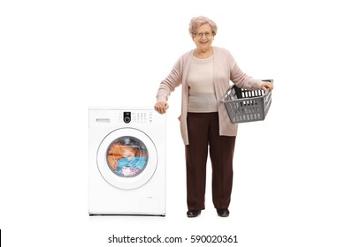 Full Length Portrait Of An Elderly Woman With An Empty Laundry Basket Standing Next To A Washing Machine Isolated On White Background