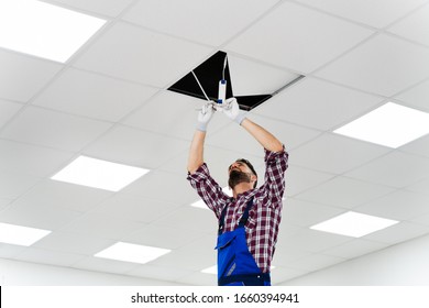 Full Length Portrait Of Electrician On Stepladder Installs Lighting To The Ceiling In Office