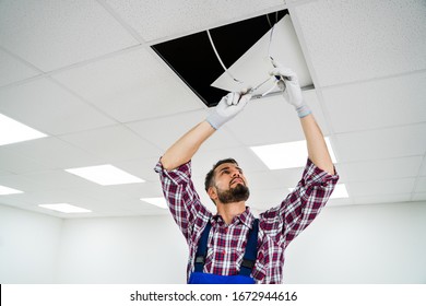 Full Length Portrait Of Electrician On Stepladder Installs Lighting To The Ceiling In Office