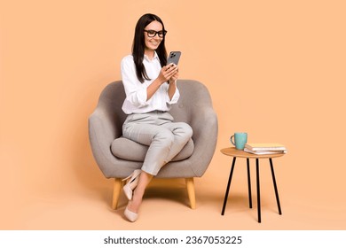 Full length portrait of elegant corporate girl sit comfort soft chair use smart phone chatting isolated on beige color background