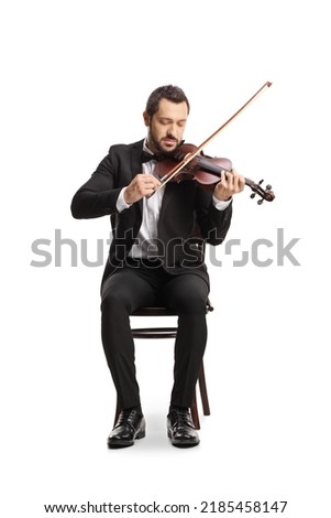 Full length portrait of an elegant young man sitting and playing a violin isolated on white background 