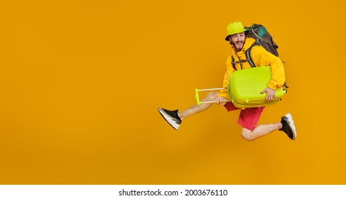 Full length portrait of emotional young hipster man jumping with backpack and suitcases. Tourism and travel, vacation. Studio portrait on a yellow background with copy space. - Shutterstock ID 2003676110