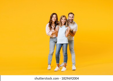 Full length portrait excited cheerful young parents mom dad with child kid daughter teen girl in t-shirts hugging looking camera isolated on yellow background. Family day parenthood childhood concept