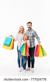 Full Length Portrait Of An Excited Family Holding Paper Shopping Bags Isolated Over White Background