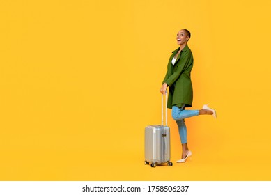 Full Length Portrait Of Excited Young African American Tourist Woman Holding Luggage On One Leg Raised Standing Gesture Ready To Travel In Isolated Studio Yellow Background