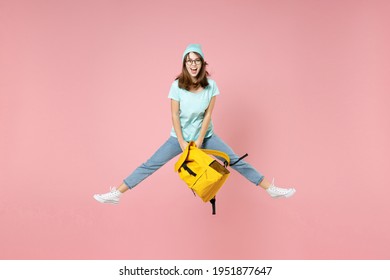 Full Length Portrait Of Excited Young Woman Student In T-shirt Hat Glasses Hold Backpack Jumping Spreading Legs Isolated On Pink Background Studio. Education In High School University College Concept