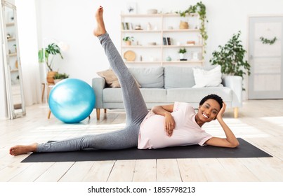 Full length portrait of expectant black woman exercising on yoga mat, lifting her leg up, feeling positive and healthy at home. Pregnant African American woman working out in living room