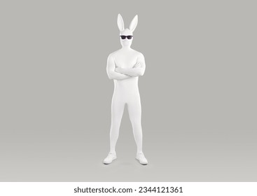 Full length portrait of faceless unrecognizable person in white spandex costume, hare mask with long ears and black glasses. Incognito funny man in bodysuit with crossed arms on grey background.