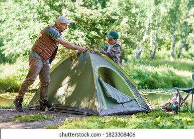 Full length portrait of father and son setting up tent together while enjoying camping in forest, copy space - Powered by Shutterstock