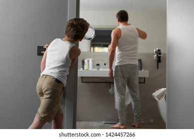 Full Length Portrait Of Father In White T-shirts Brushing His Teeth While Little Son Turning Off Light In Bathroom