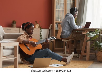 Full length portrait of female African-American musician playing guitar and using laptop while sitting on floor in recording studio, copy space - Powered by Shutterstock