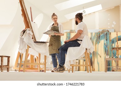 Full length portrait of female artist painting picture on easel while working in sunlit art studio with bearded man sitting on chair and posing, copy space - Powered by Shutterstock