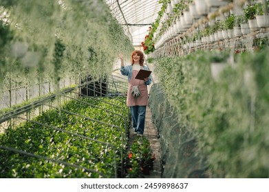 Full length portrait of female florist standing at greenhouse surrounded by flowers and plants with clipboard in hands and taking care of greenery. Small business owner inventorying pots of flowers. - Powered by Shutterstock