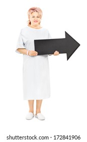 Full Length Portrait Of Female Patient In Hospital Gown Holding Big Black Arrow Pointing Right Isolated On White Background