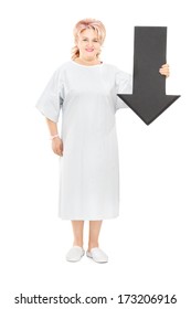 Full Length Portrait Of Female Patient In Hospital Gown Holding Big Black Arrow Pointing Down Isolated On White Background