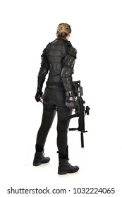 full length portrait of female  soldier wearing black  tactical armour  holding a gun, facing away from camera, isolated on white studio background.