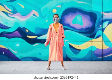 Full length portrait of female street artist in respirator mask standing near the graffiti wall with her paintings looking to camera. Urban art concept - Powered by Shutterstock